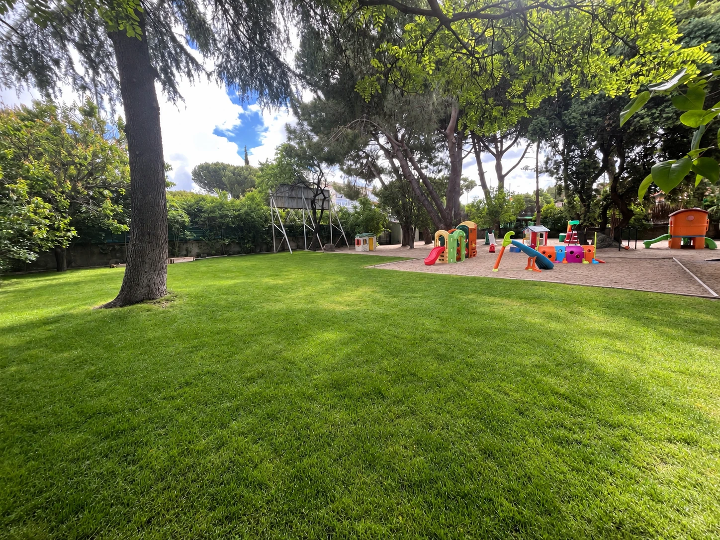 Zona exterior de Cascarón Galapagar, con jardín arbolado y juegos infantiles sobre arena.